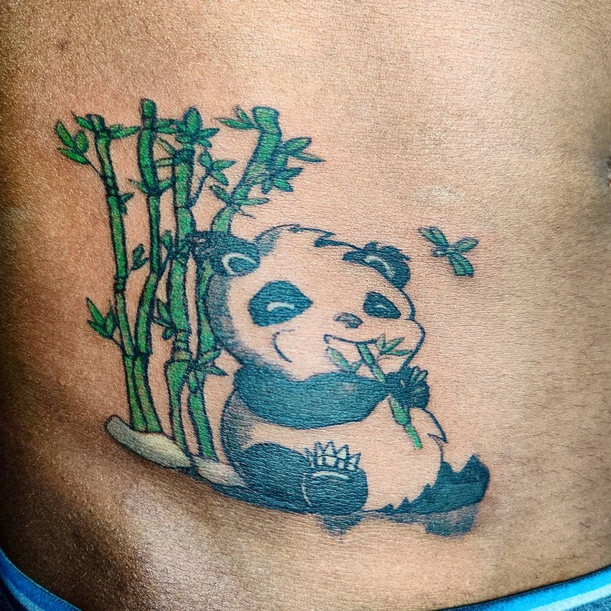 Close-up of a panda tattoo with green bamboo and a small butterfly on skin